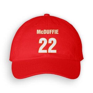Può includere: Cappellino da baseball rosso con testo bianco che dice "McDuffie 22" in un contorno giallo.