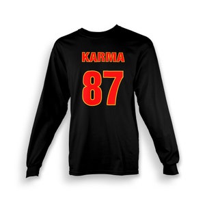 Op de afbeelding: Zwart shirt met lange mouwen met het woord "KARMA" en het nummer "87" gedrukt in rood met een gele omtrek.