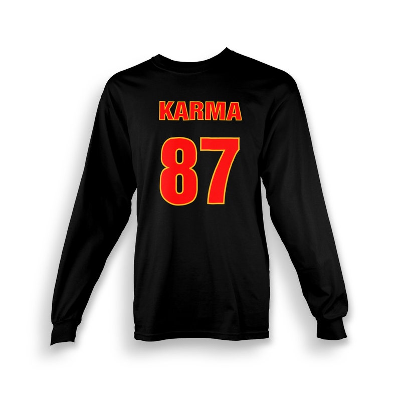 Op de afbeelding: Zwart shirt met lange mouwen met het woord "KARMA" en het nummer "87" gedrukt in rood met een gele omtrek.