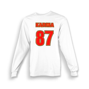 Op de afbeelding: Witte longsleeve t-shirt met het woord "KARMA" en het nummer "87" gedrukt op de rug in rood met een gele omtrek.