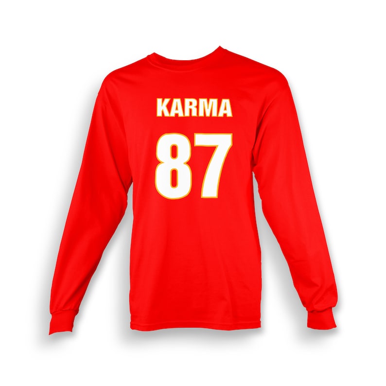 Op de afbeelding: Rood longsleeve shirt met het woord "KARMA" en het nummer "87" gedrukt in wit met een gele omtrek.