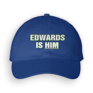 May include: A royal blue baseball cap with white text that reads "EDWARDS IS HIM" in a green outline.