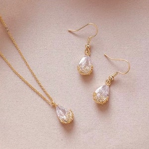May include: A gold necklace and earrings set with teardrop-shaped crystal pendants. The pendants are surrounded by a delicate gold filigree design.