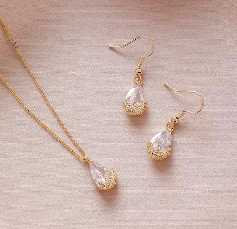 May include: A gold necklace and earrings set with teardrop-shaped crystal pendants. The pendants are surrounded by a delicate gold filigree design.
