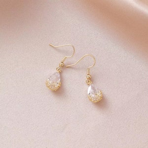 May include: A pair of gold teardrop earrings with clear crystal stones. The earrings have a delicate, intricate design.
