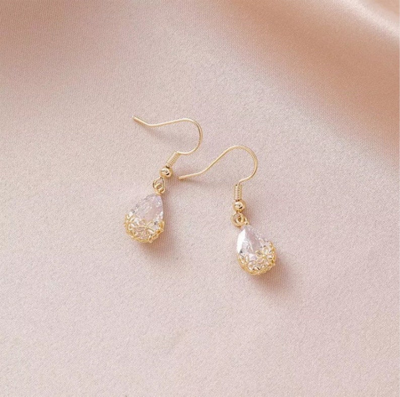 May include: A pair of gold teardrop earrings with clear crystal stones. The earrings have a delicate, intricate design.