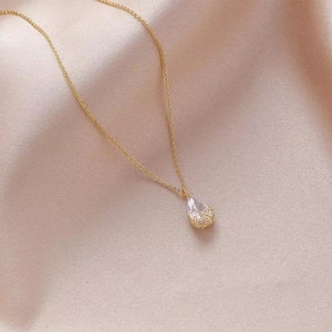 May include: A delicate gold chain necklace with a teardrop-shaped crystal pendant. The crystal is clear and has a faceted design.