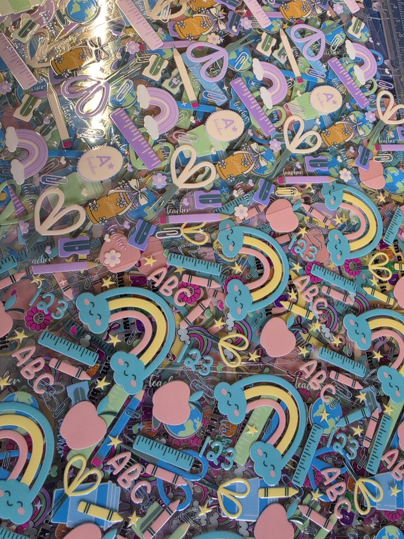 May include: A collection of school-themed stickers featuring pastel-colored rainbows with clouds, rulers, pencils, apples, scissors, and the letters ABC and 123. The designs include various educational icons in shades of blue, pink, yellow, and purple.
