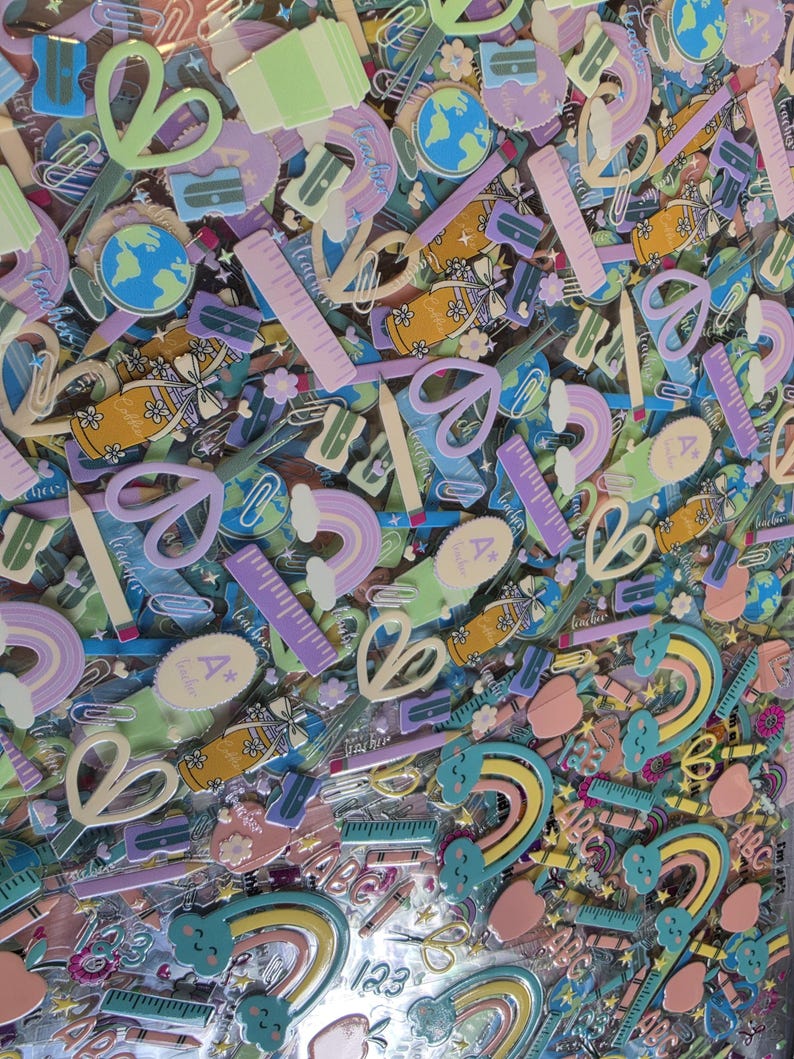 May include: A collection of school-themed stickers featuring pastel-colored illustrations of scissors, rulers, pencils, globes, rainbows, apples, and jars. The designs include text elements like A+ teacher, 123, and ABC in a variety of soft hues.