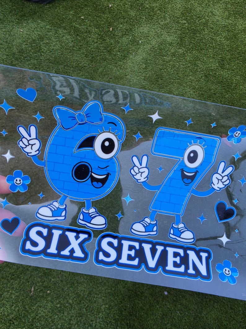 May include: A clear decal featuring a blue cartoon number six with a bow and a blue cartoon number seven, both with arms, legs, and sneakers making peace signs. The design includes blue hearts, flowers, and stars with the text SIX SEVEN below.