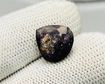 May include: A dark, iridescent gemstone with a faceted, heart-shaped cut. The stone has a deep, rich color with hints of gold and pink.