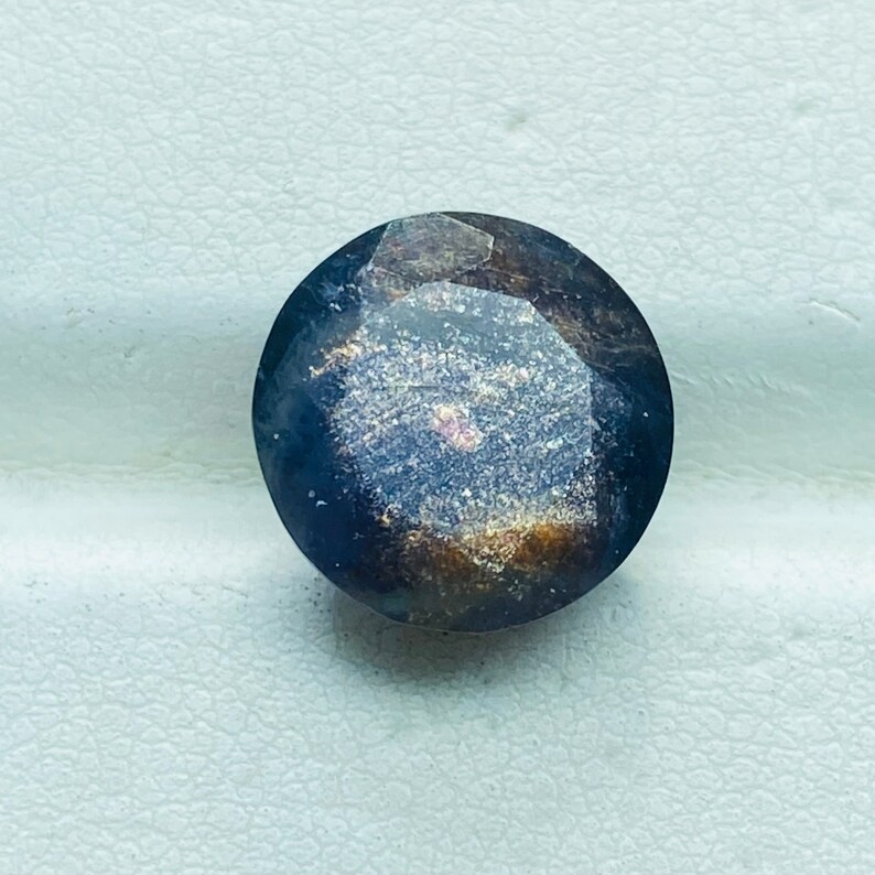 Pu&ograve; includere: Una pietra preziosa rotonda di colore blu scuro con taglio sfaccettato e finitura scintillante e iridescente.