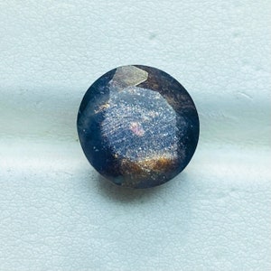 Pu&ograve; includere: Una pietra preziosa rotonda di colore blu scuro con taglio sfaccettato e un tocco di lucentezza dorata e rosata.