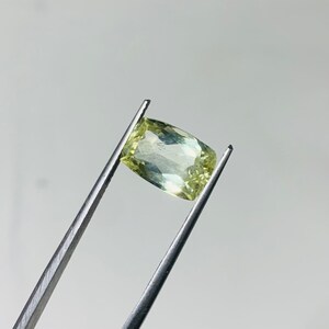May include: A light green gemstone with a rectangular shape, held in tweezers.