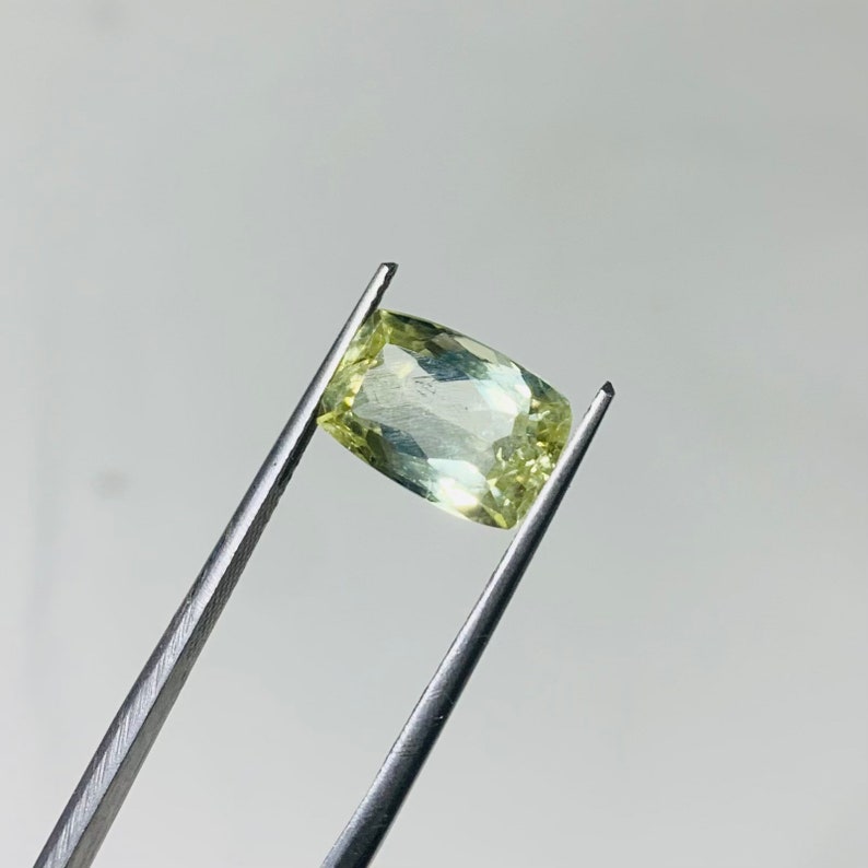 May include: A light green gemstone with a rectangular shape, held in tweezers.