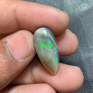 May include: A teardrop-shaped opal cabochon with a light gray base and flashes of green, blue, and orange.