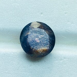 Pu&ograve; includere: Una pietra preziosa rotonda, sfaccettata, di colore blu scuro con una finitura scintillante e iridescente.