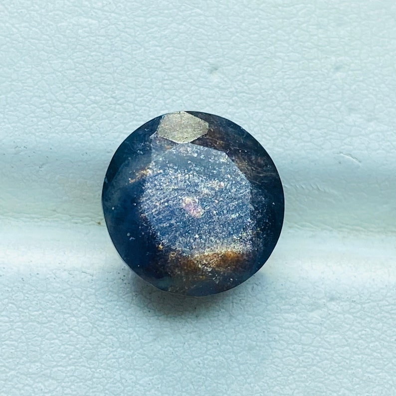 Pu&ograve; includere: Una pietra preziosa rotonda, sfaccettata, di colore blu scuro con una finitura scintillante e iridescente.