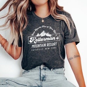 Op de afbeelding: Een donkergrijs heather t-shirt met een wit grafisch ontwerp met een bergketen en de tekst "Come Have the Time of Your Life Kellerman's Mountain Resort Catskills New York".