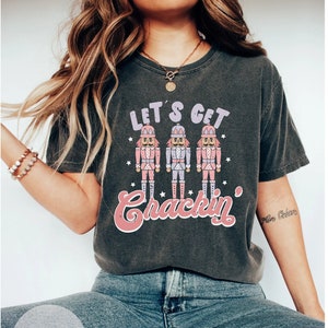 May include: A grey t-shirt with a vintage-style graphic of three nutcrackers and the text "Let's Get Crackin'".