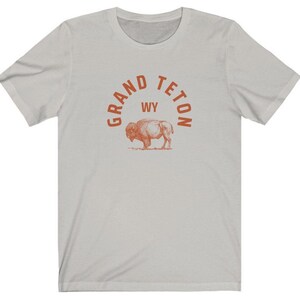 May include: A light gray t-shirt with an orange graphic print of a bison and the text "GRAND TETON WY" in an arc above the bison.