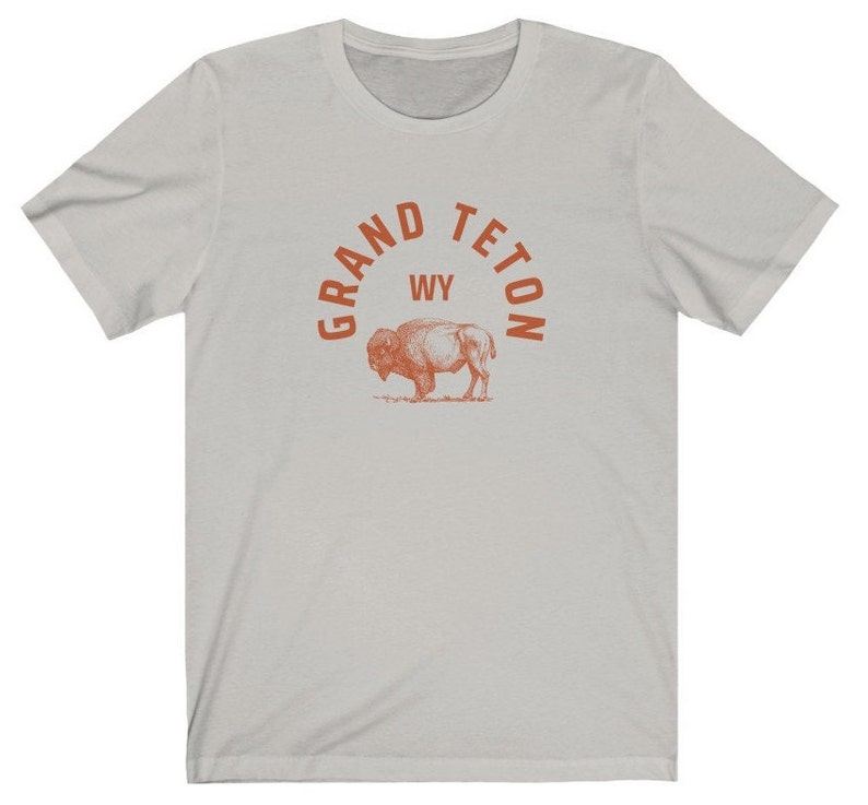 May include: A light gray t-shirt with an orange graphic print of a bison and the text "GRAND TETON WY" in an arc above the bison.