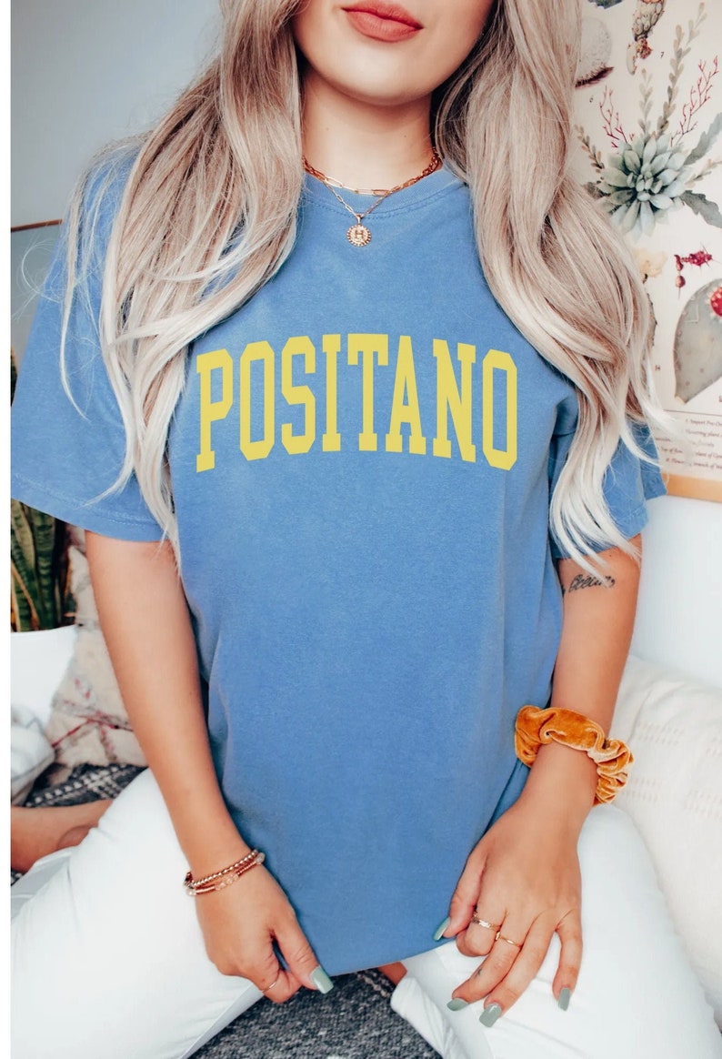 May include: A blue t-shirt with the word "POSITANO" printed in yellow on the front.