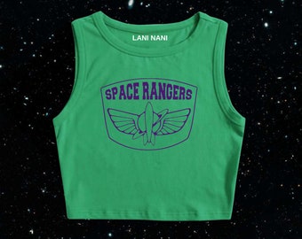 Könnte beinhalten: Grünes ärmelloses Crop-Top mit einer lila Grafik eines Raumschiffs und dem Text "SPACE RANGERS" sowie dem Text "LANI NANI" oben.