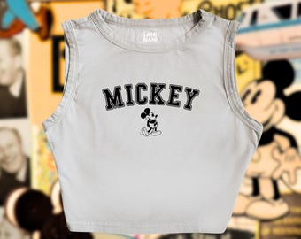 Op de afbeelding: Een lichtgrijs, mouwloos crop top met een zwarte Mickey Mouse-afbeelding en de tekst "MICKEY" in zwart.