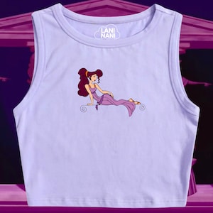 May include: A lavender sleeveless crop top with a graphic print of a cartoon woman in a purple dress. The text "Lani Nani" is printed on the top in a white cloud.