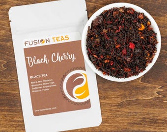 以下が含まれることがあります： 「FUSION TEAS Black Cherry BLACK TEA Black Tea, Hibiscus Blossoms, Rose Hips, Safflower, Cranberries, Raisins, Flavor www.fusionteas.com」と書いてある茶色のラベルが付いた白いポーチ。ポーチの隣には、赤い果実とオレンジ色の果実が入った茶葉の黒茶がたっぷり入った白いボウルがある。