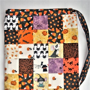 May include: A patchwork Halloween drawstring bag with a black and white cat, orange and black bats, candy corn, pumpkins, and mice designs. The bag is made of fabric and has a drawstring closure.