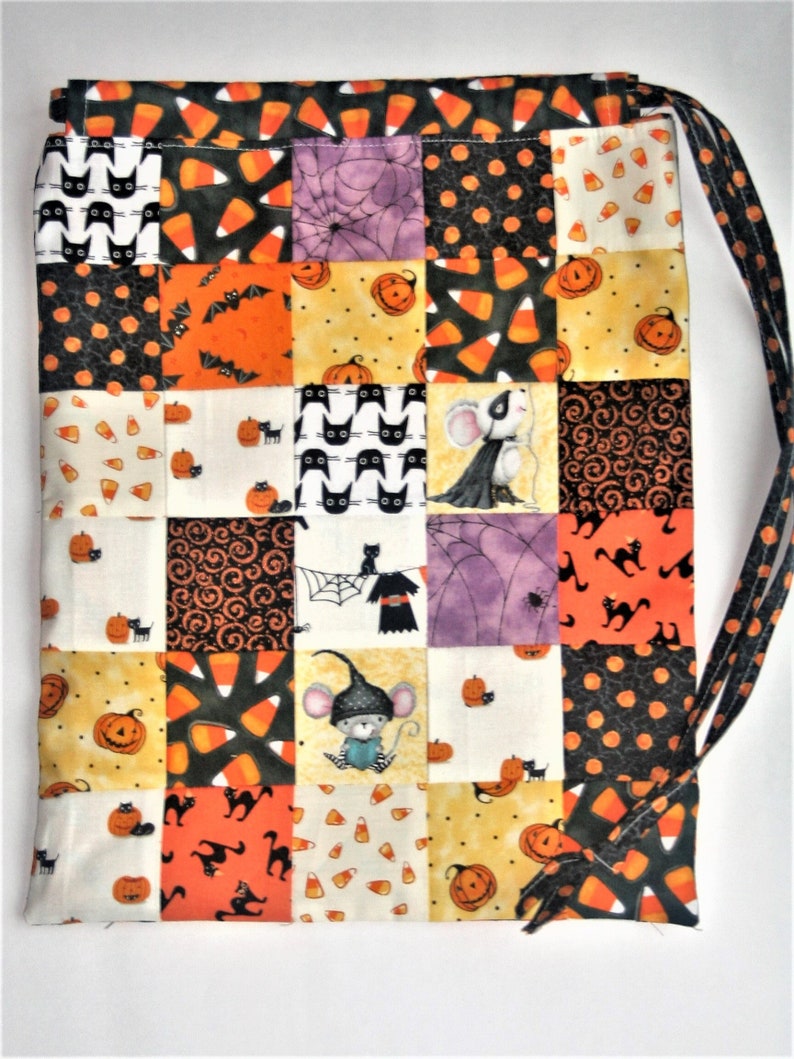 May include: A patchwork Halloween drawstring bag with a black and white cat, orange and black bats, candy corn, pumpkins, and mice designs. The bag is made of fabric and has a drawstring closure.