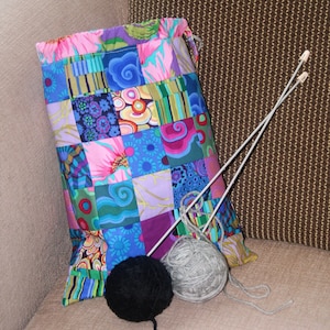 May include: A patchwork fabric drawstring bag with a colorful design. The bag is filled with yarn and knitting needles.