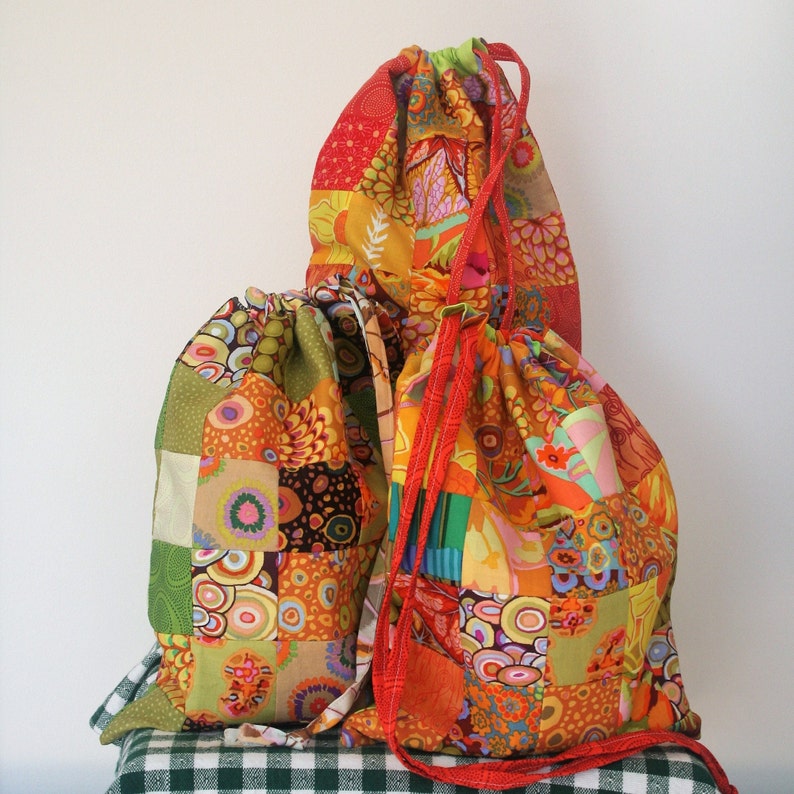 May include: Three colorful drawstring bags made of patchwork fabric. The bags are in shades of orange, yellow, green, and brown. The bags are made of different patterns and fabrics, and they are all tied together with a drawstring.