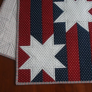 May include: Red, white, and blue fabric table runner with a star pattern. The runner has a white background with red and blue stripes along the edges.