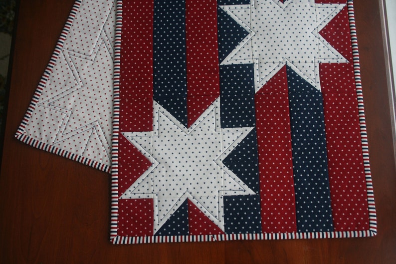 May include: Red, white, and blue fabric table runner with a star pattern. The runner has a white background with red and blue stripes along the edges.