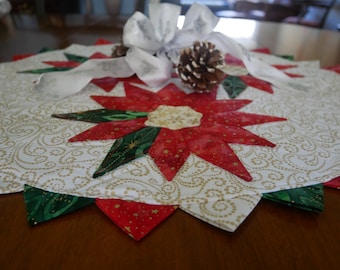 Peut inclure: Un chemin de table blanc avec un motif de spirales dorées et un design de poinsettia rouge et vert. Le chemin de table est décoré d'un nœud blanc et d'une pomme de pin.
