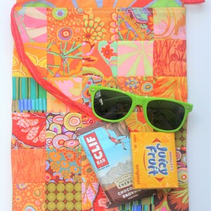 May include: A patchwork fabric drawstring bag with a red strap, green sunglasses, a Clif Bar energy bar, and a Juicy Fruit gum pack. The bag is made of colorful fabric with a variety of patterns.