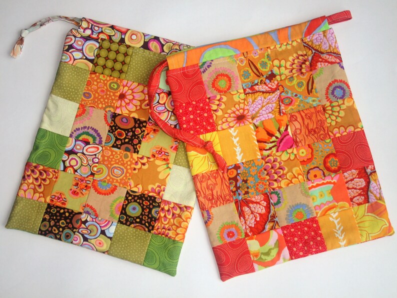 May include: Two colorful patchwork fabric drawstring bags with a variety of floral and geometric patterns in shades of orange, red, green, brown, and yellow.