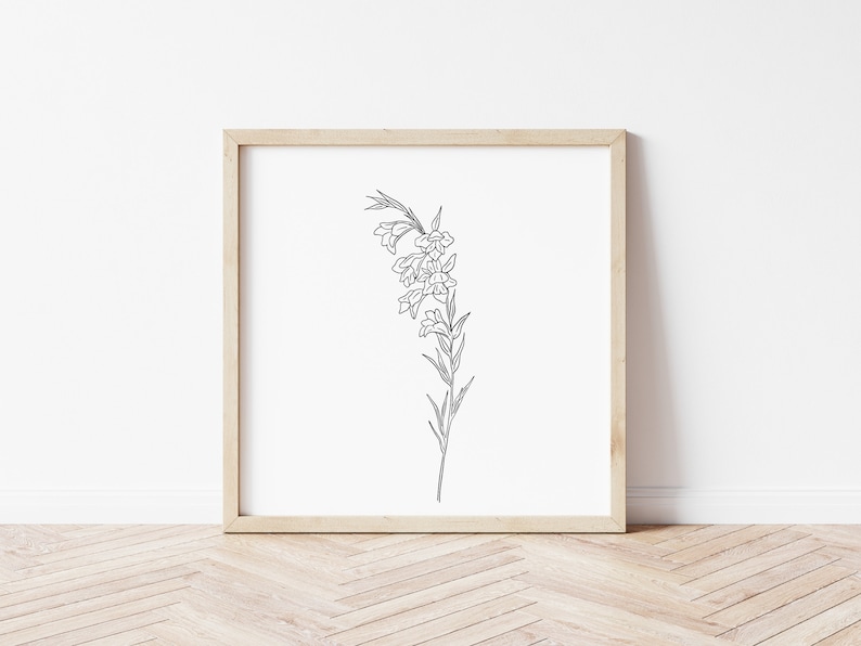 Op de afbeelding: Een zwart-witte lijntekening van een bloem met delicate bloemblaadjes en bladeren, ingelijst in een licht houten frame.