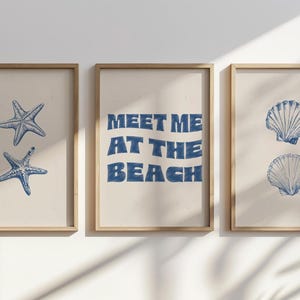 May include: Three framed prints with a beach theme. The left print features two blue starfish, the centre print has the text "MEET ME AT THE BEACH" in blue, and the right print displays two blue seashell illustrations.