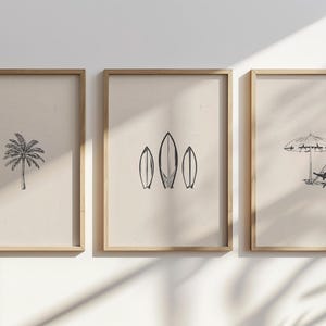 Pode incluir: Três impressões emolduradas com um tema de praia. A primeira impressão apresenta uma palmeira, a segunda impressão apresenta três pranchas de surf e a terceira impressão apresenta um guarda-sol de praia e uma cadeira de praia.