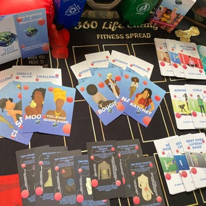 Op de afbeelding: Een set kleurrijke fitnesskaarten met illustraties en tekst. De kaarten tonen verschillende oefeningen, waaronder planken, intervallen en rekoefeningen. De kaarten liggen op een zwart en gouden oppervlak.