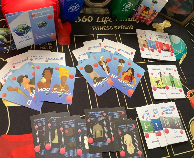 Op de afbeelding: Een set kleurrijke fitnesskaarten met illustraties en tekst. De kaarten tonen verschillende oefeningen, waaronder planken, intervallen en rekoefeningen. De kaarten liggen op een zwart en gouden oppervlak.