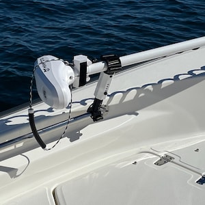 Puede incluir: Un motor de pesca el&eacute;ctrico blanco montado en un barco blanco. El motor est&aacute; unido a un brazo de metal blanco que se extiende desde el barco. El motor tiene una etiqueta en blanco y negro que dice "Trolling Motor".