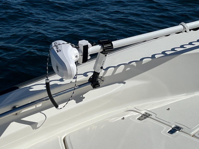 Puede incluir: Un motor de pesca el&eacute;ctrico blanco montado en un barco blanco. El motor est&aacute; unido a un brazo de metal blanco que se extiende desde el barco. El motor tiene una etiqueta en blanco y negro que dice "Trolling Motor".