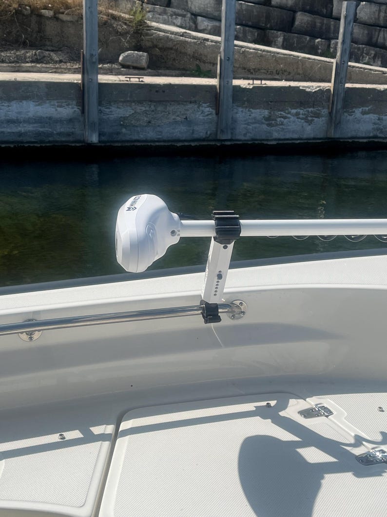 Puede incluir: Un motor de pesca el&eacute;ctrico blanco montado en un barco blanco con una barandilla plateada. El motor est&aacute; conectado a un brazo de metal blanco que est&aacute; conectado a la barandilla.