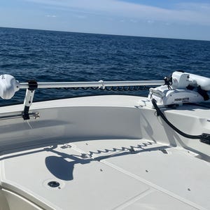 Puede incluir: Un motor de pesca el&eacute;ctrico Minn Kota blanco montado en la parte trasera de un barco. El motor est&aacute; extendido y el barco est&aacute; en el agua.