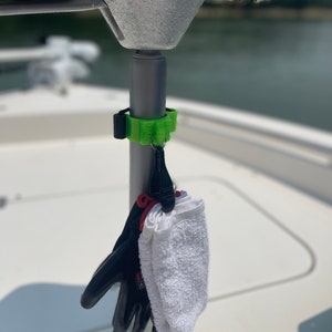 Peut inclure: Un crochet en plastique vert fixé à un poteau métallique sur un bateau. Une serviette blanche et des gants noirs sont accrochés au crochet.